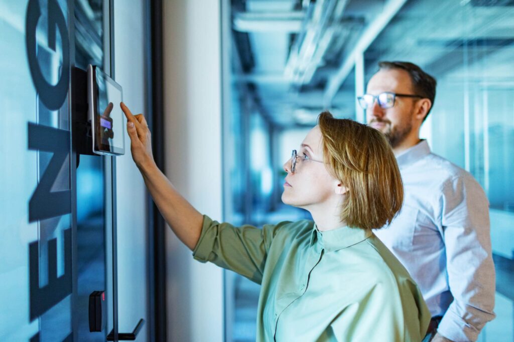 Colleagues leveraging touchscreen technology to seamlessly control meeting room access, highlighting modern technology integration in collaborative workspaces.