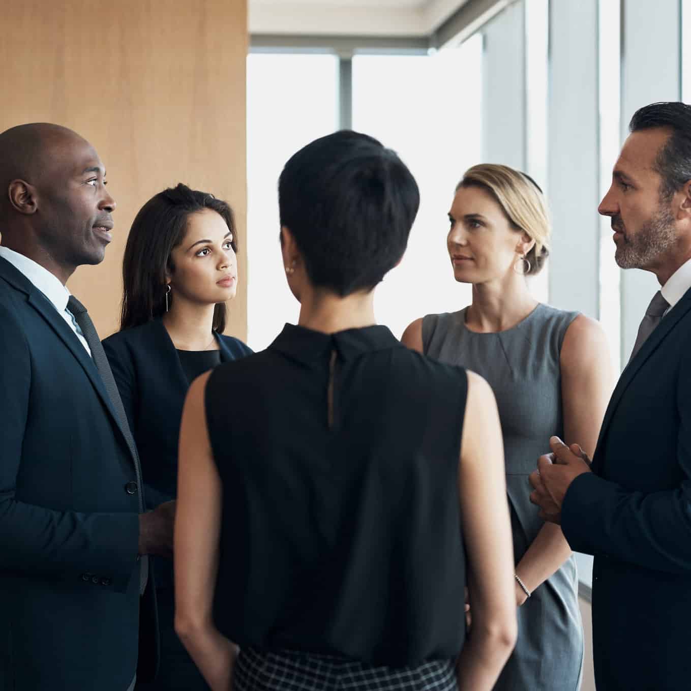 Five professionals discuss M&A Integration Consulting in a bright, modern office setting.