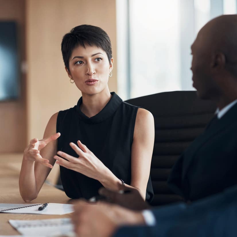 Woman in black top gestures while discussing trial strategy consulting at a business meeting.