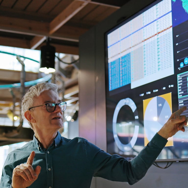 Man pointing at data charts on a large display screen during a presentation.