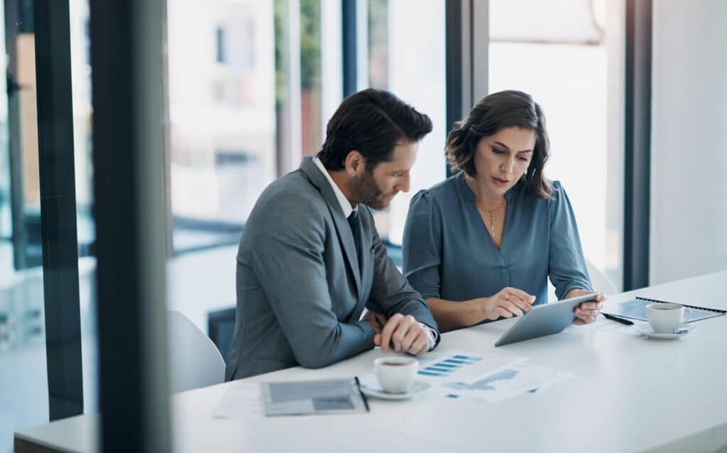 Two business professionals discuss law firm pricing strategy consulting over data and coffee.