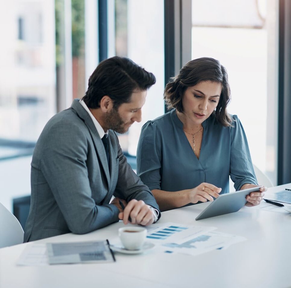 Two business professionals discuss law firm pricing strategy consulting over data and coffee.