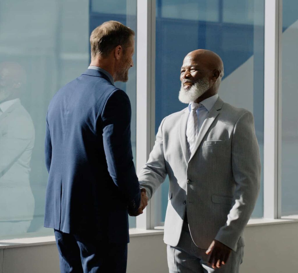 Two men in suits smiling and shaking hands after Law Firm Client Retention Strategy consulting.