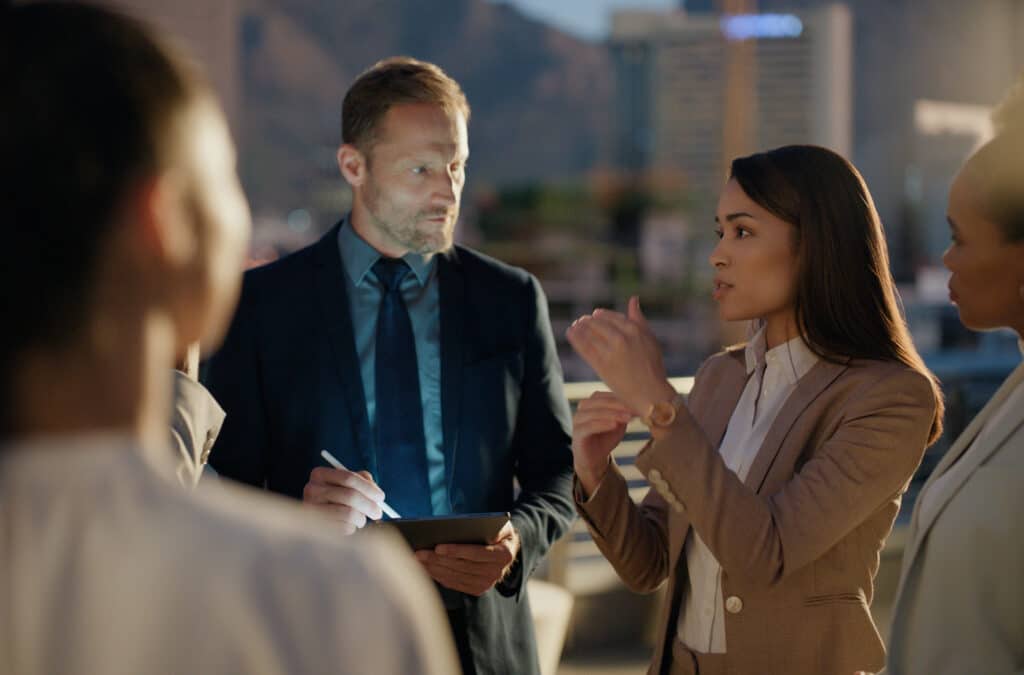 Law firm consultants discuss business outdoors in the evening with city buildings behind them.