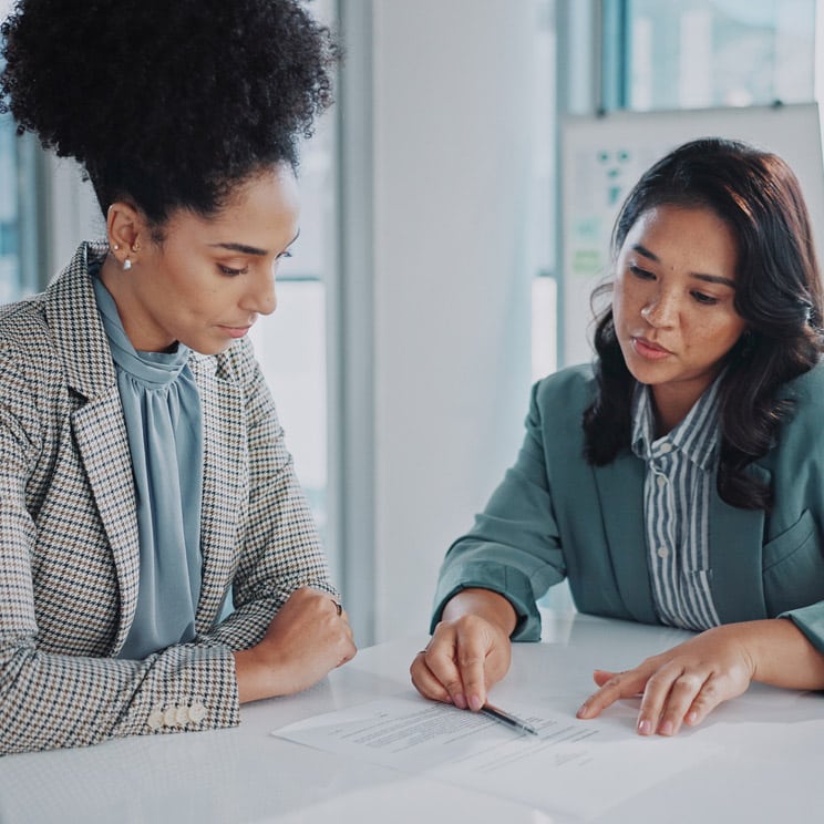 Two women in business attire, likely Witness Preparation Consultants, discussing a document.