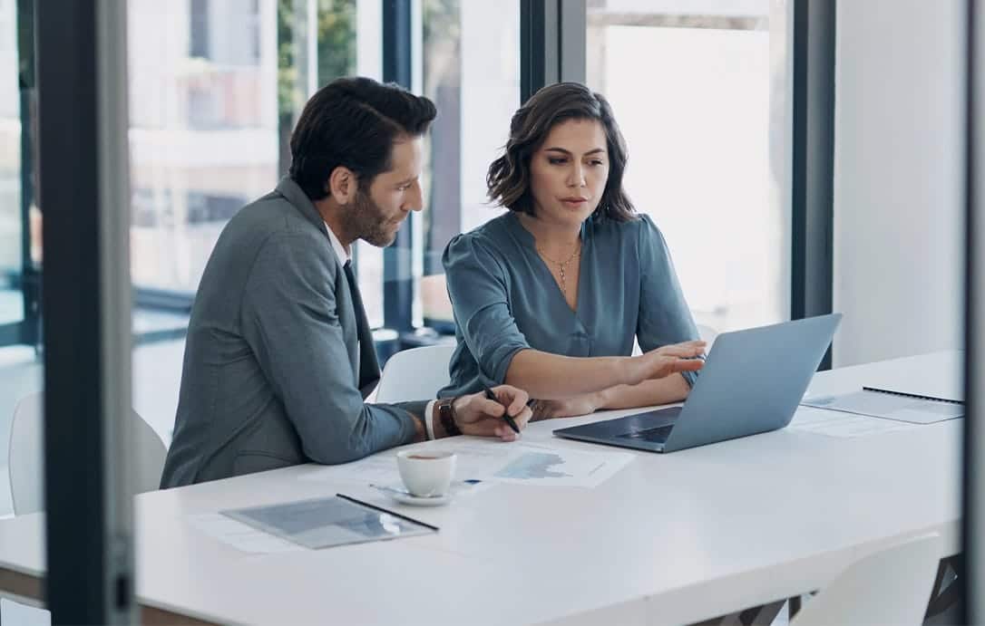 Business man, woman and laptop in discussion for deal, agreement and proposal for b2b collaboration. People, computer and meeting with paperwork for financial strategy, stats or negotiation in office