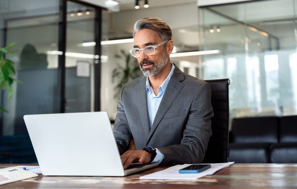 Businessman using computer, typing, working in modern office, doing online data market analysis, thinking planning tech strategy looking at laptop with copy space.