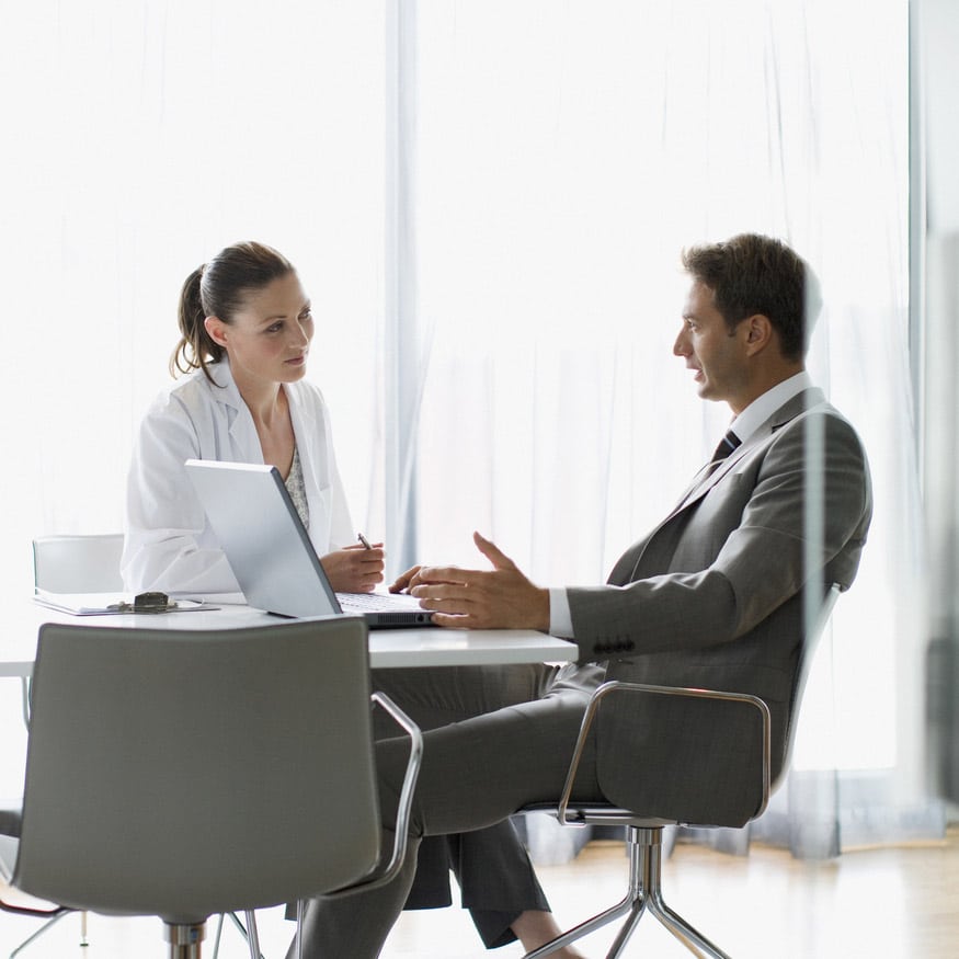 A doctor and a man in a suit discuss Healthcare Litigation Support at a desk in a bright office.