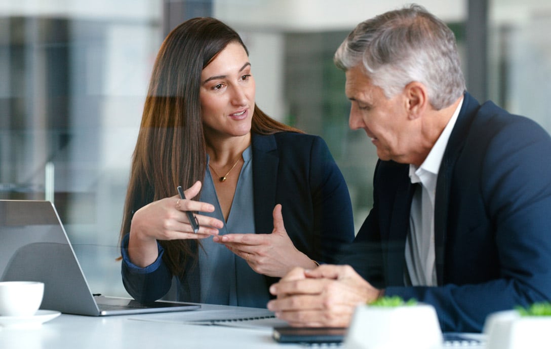 Two business professionals discuss Law Firm Client Relationship Management (CRM) Consulting at desk.
