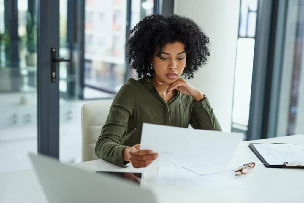 Woman sitting at desk, reading documents, pondering Document Management Consulting solutions.