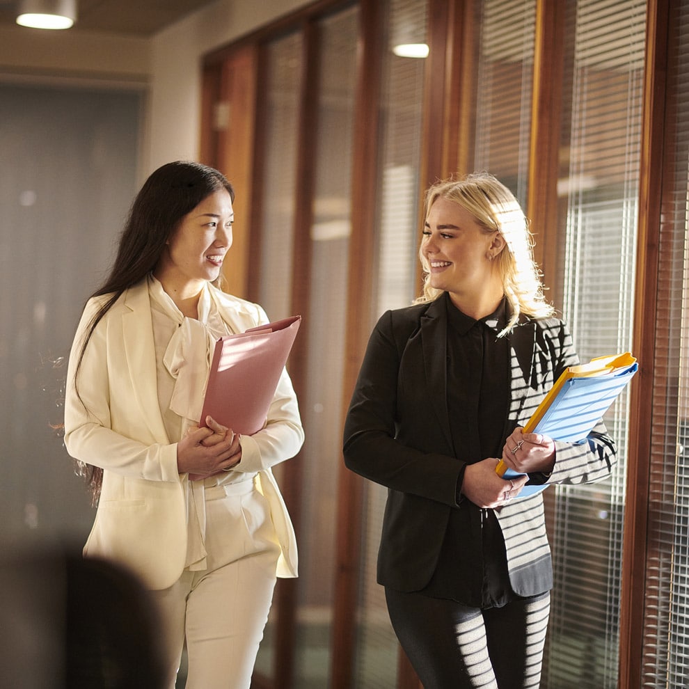 Two women in business attire discuss Law Firm Consulting while walking in an office hallway.