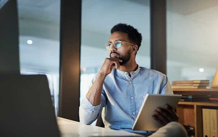 Man with glasses holding a tablet, pondering high-value customer acquisition at his desk.