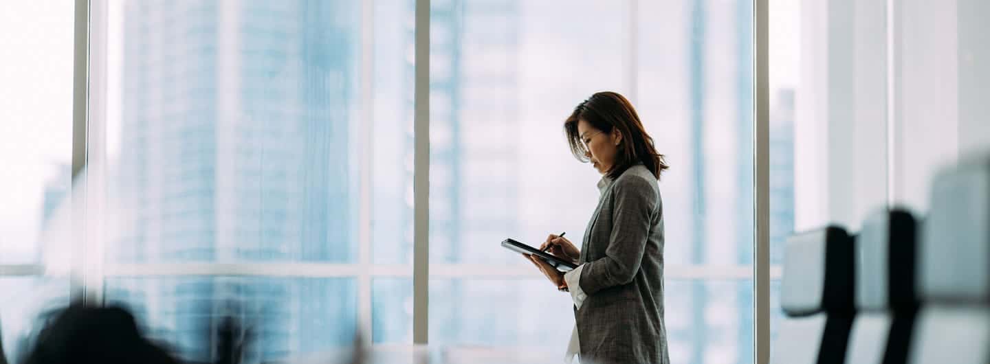 An Asian businesswoman holding digital tablet and look in distance window thinking or planning future success, thoughtful motivated mature businesswoman pondering over new ideas.