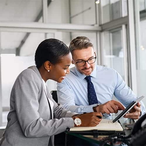 Two business professionals discuss work and review CRE Corporate Performance Consulting data.