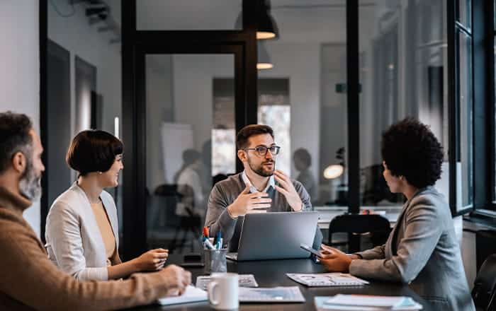 Four people discuss Hotel & Hospitality Branding with Neuroscientific Insights in a modern office.