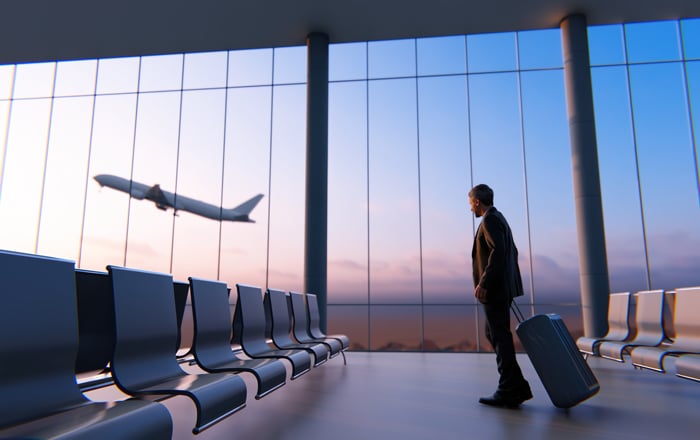 Man with suitcase watches plane take off, pondering predictive analytics for booking.