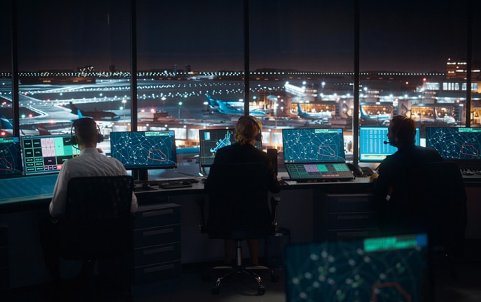 Three air traffic controllers monitor screens in a control tower—Travel & Hospitality IT Consulting.