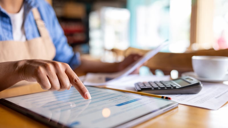Person using a tablet at a desk, managing papers for Law Firm Expense Management Consulting.