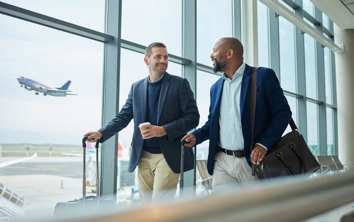 Two men in suits walk with luggage—aviation organization seen outside, consulting on human capital.