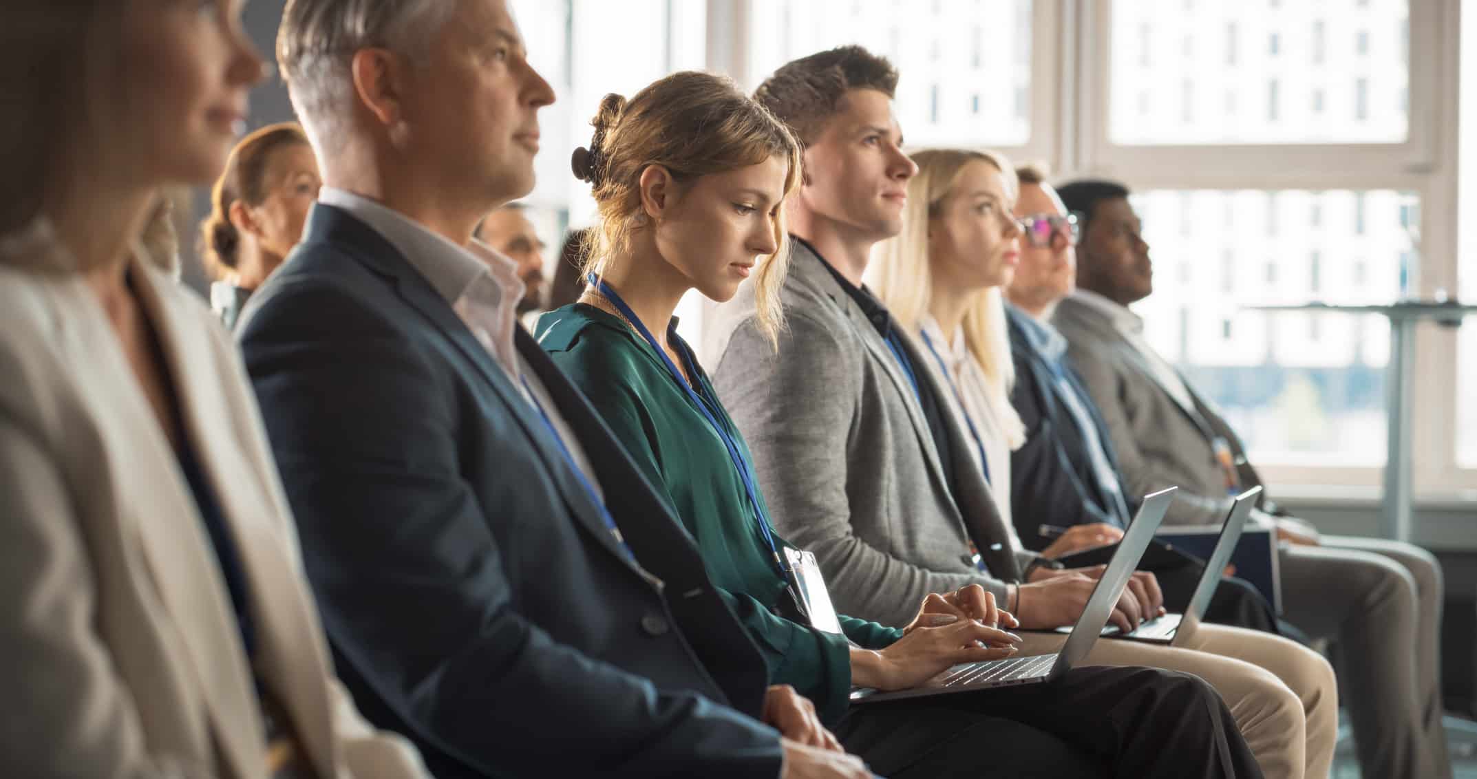 People sit in rows at a High Tech Corporate Performance Consulting conference listening attentively.