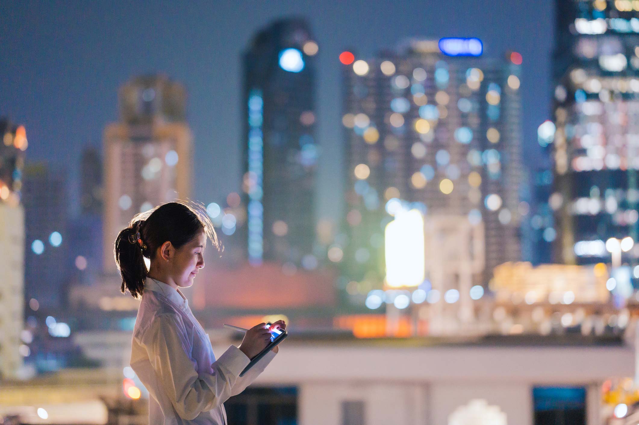 Woman using tablet at night, city lights aglow—Financial Services Strategy & Innovation Consulting.