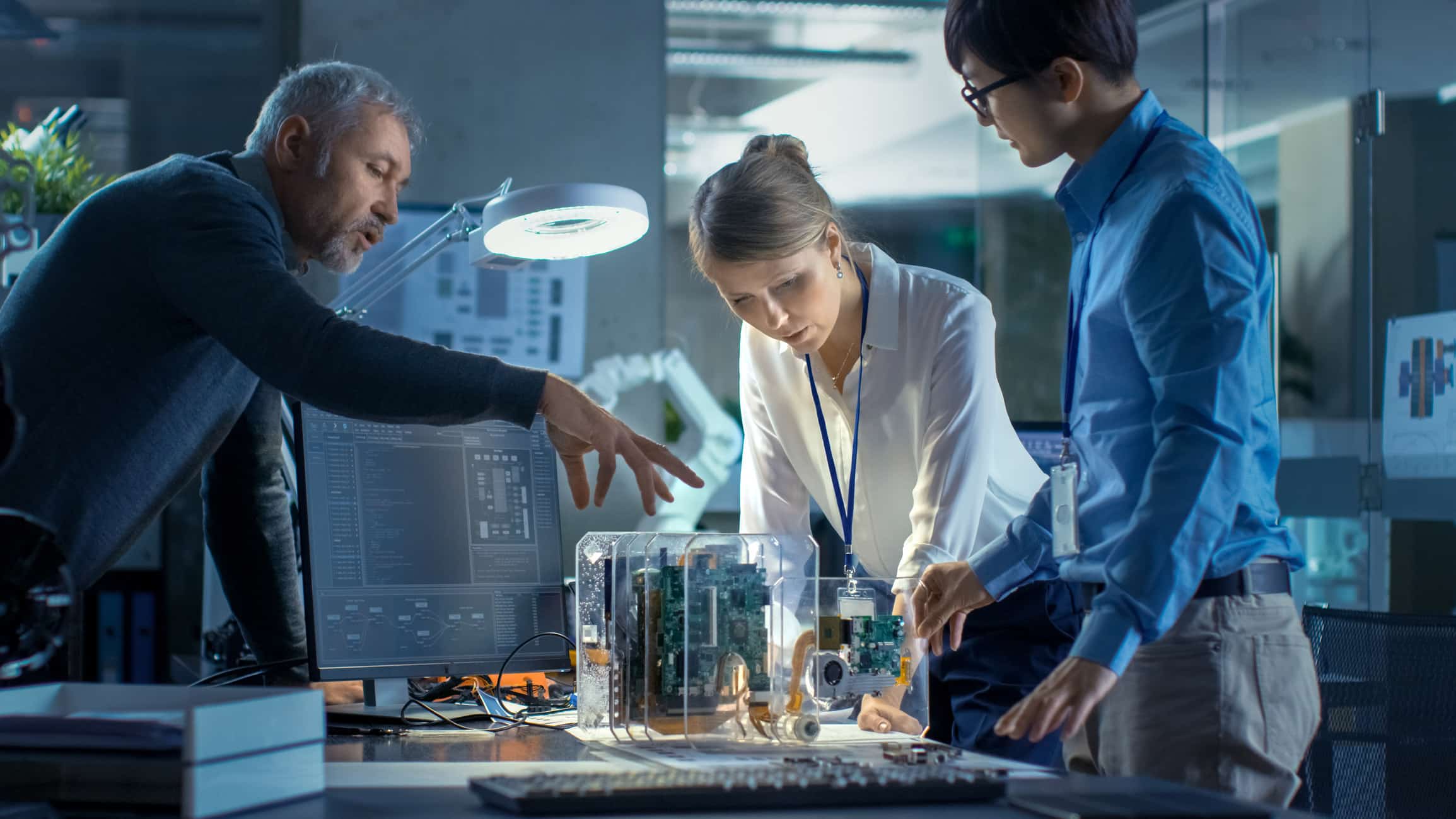 Three people collaborate on a circuit board project, exploring manufacturing digital transformation.