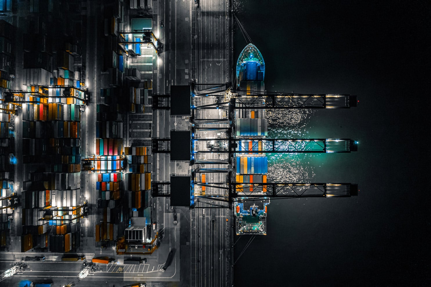 Aerial night view of a cargo ship docked at a port with colorful shipping containers.