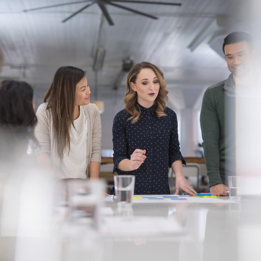 Three people discuss documents in an office, exploring Continuous Active Learning (CAL) Consulting.