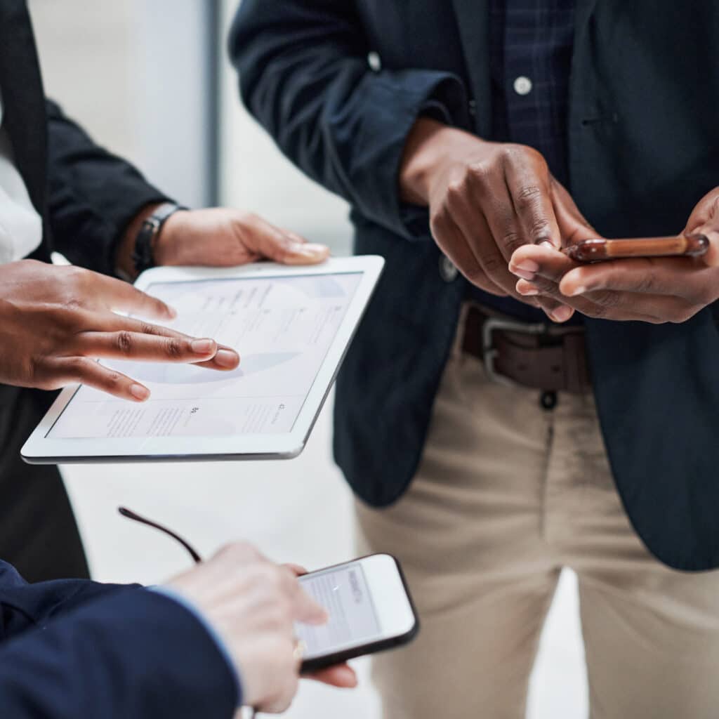 Three people using a tablet and smartphones in a Risk Management Consulting setting.