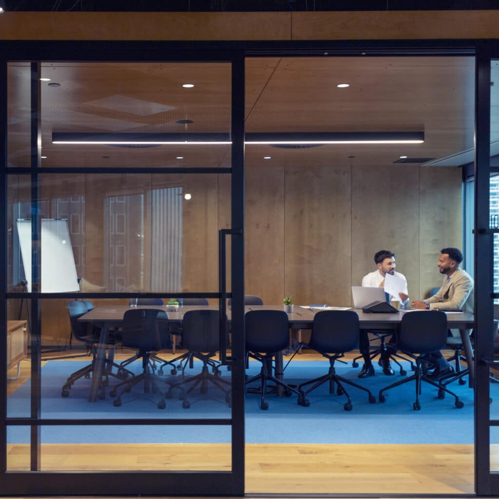 Two men discussing Corporate Tax Consulting in a modern glass-walled conference room.