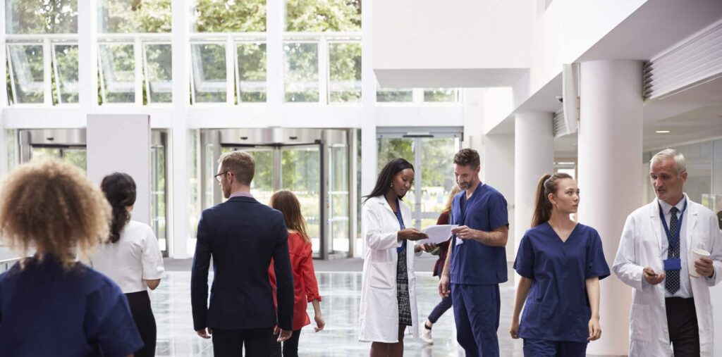 Doctors, nurses, and professionals walking and talking in a bright hospital lobby.