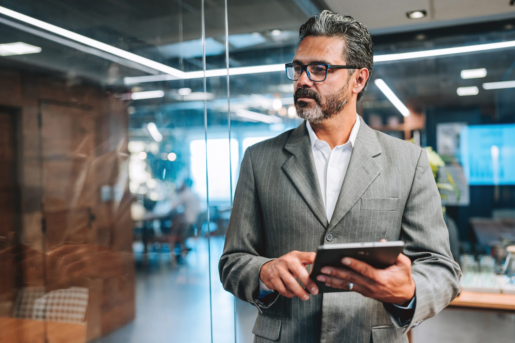 Man in a suit holding a tablet, contemplating law firm client retention strategy in modern office.