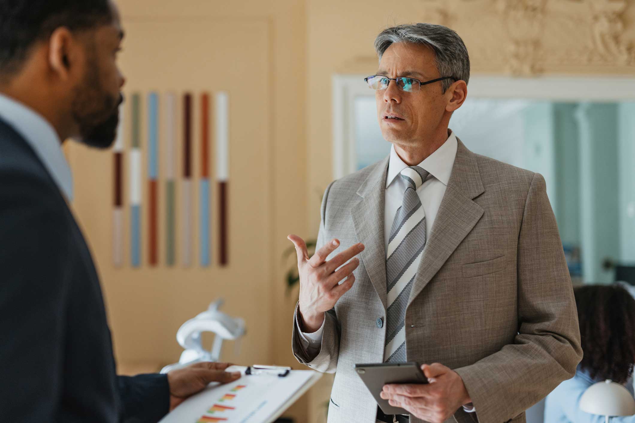 Two men in suits discuss information security advisory; one holds a clipboard, the other a tablet.
