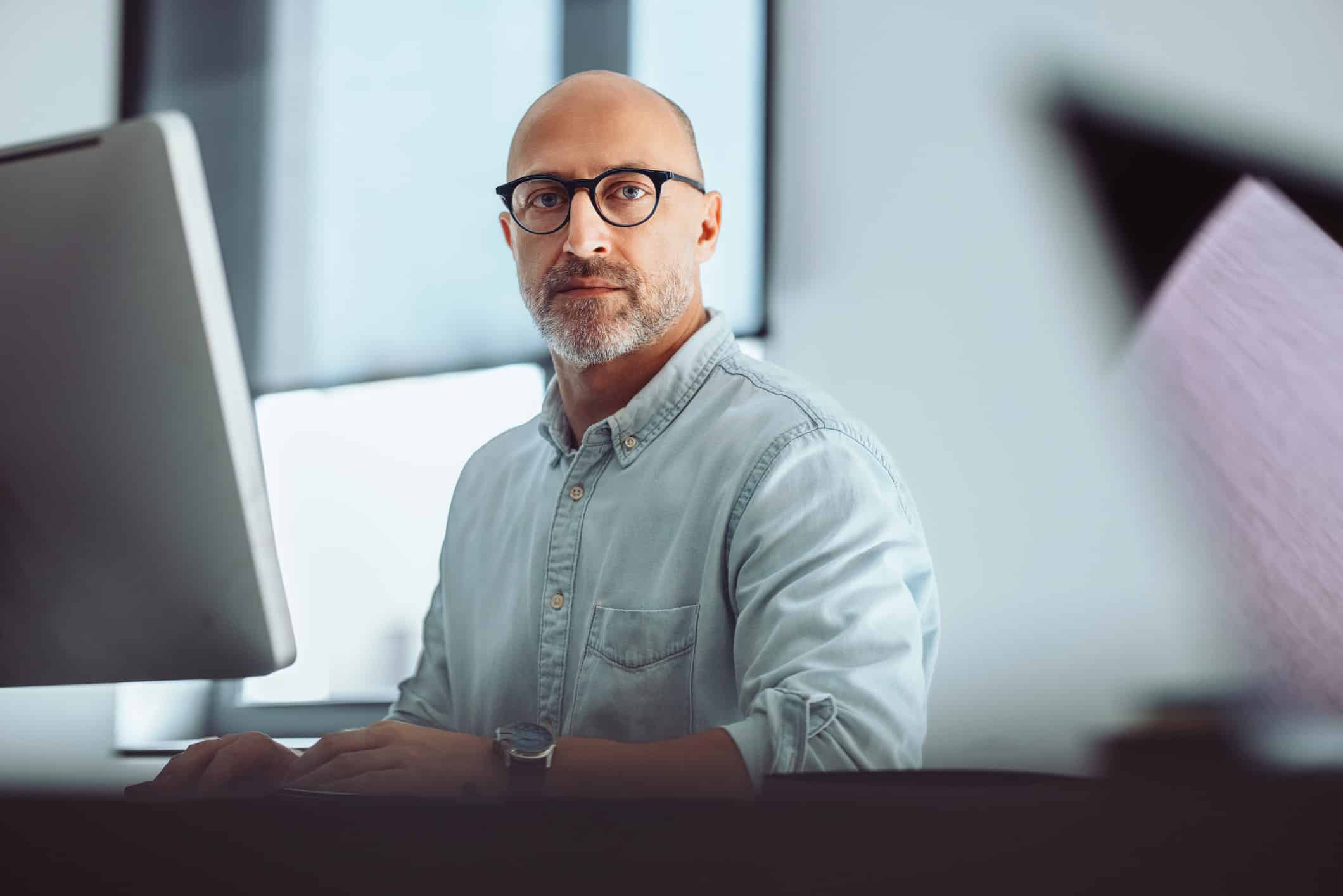 Bald man with glasses working at a computer on Securities Litigation Consulting in a bright office.