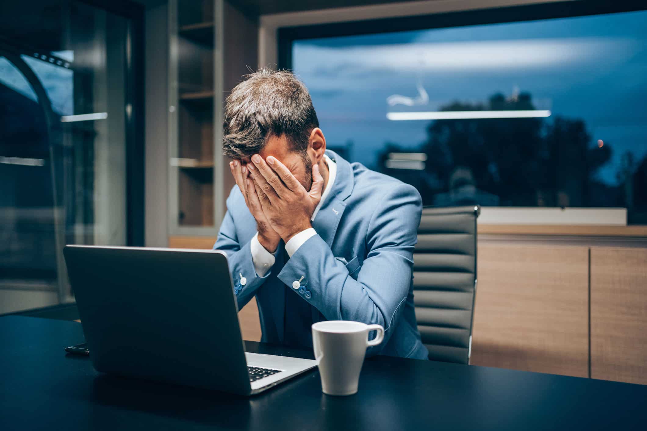 Stressed man in suit at desk highlights need for employee wellness consulting.