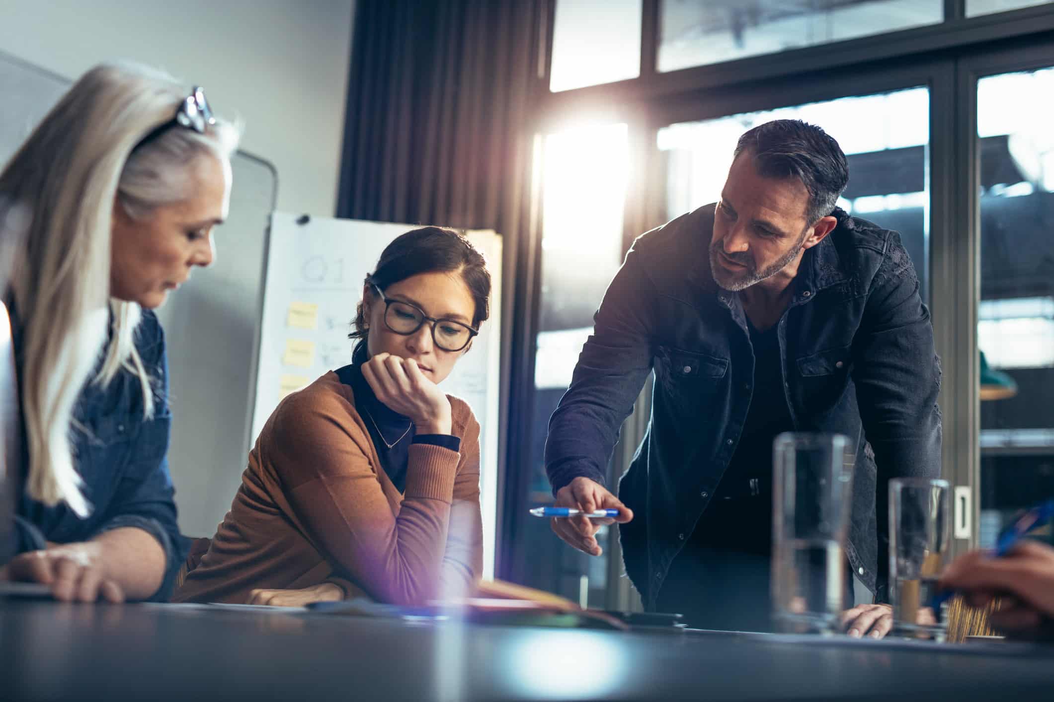 Three people in meeting at Risk Management Consulting Firm, discussing documents in a modern office.