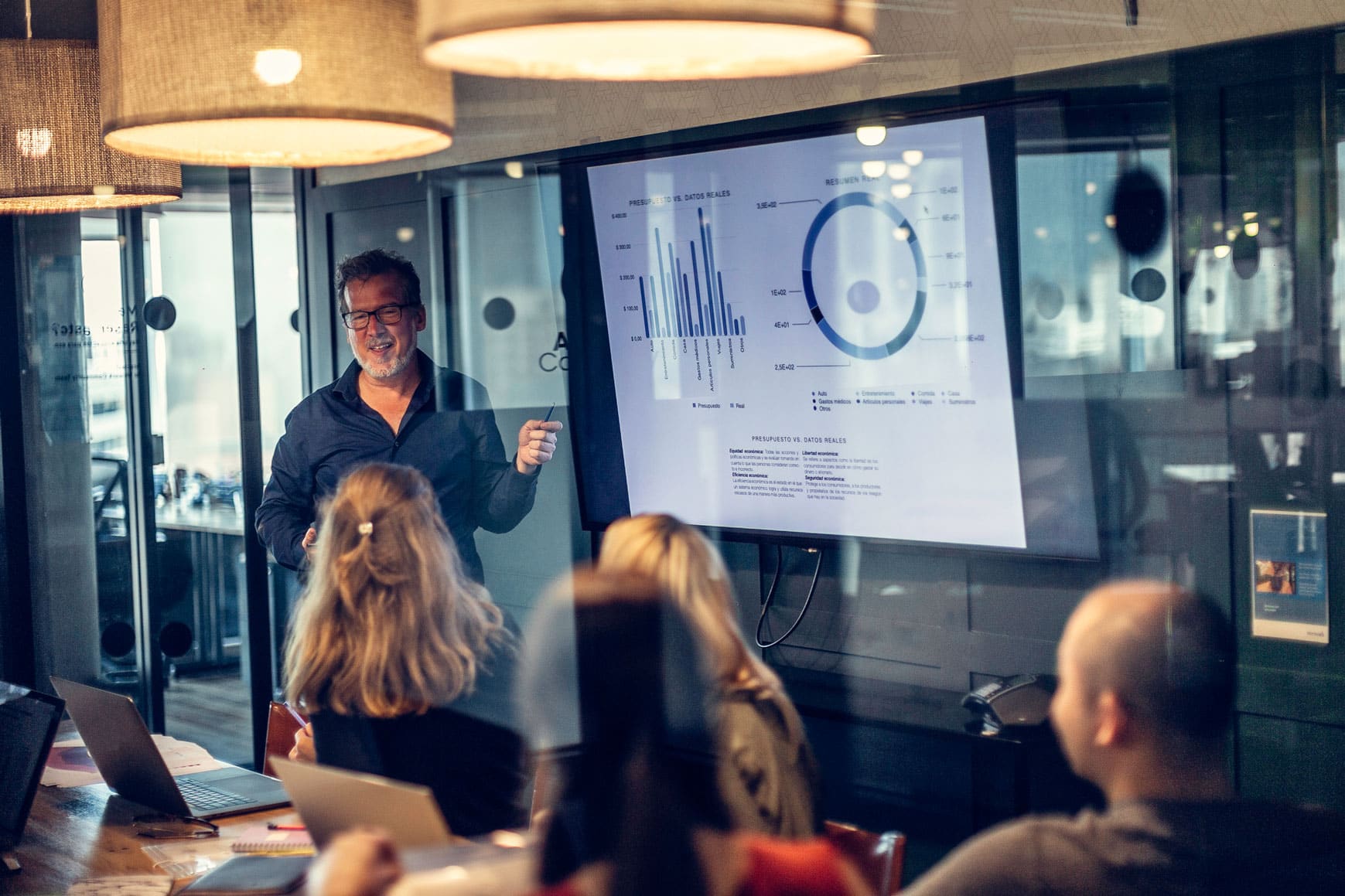Man presenting data charts and statistical modeling to colleagues in a modern glass conference room.