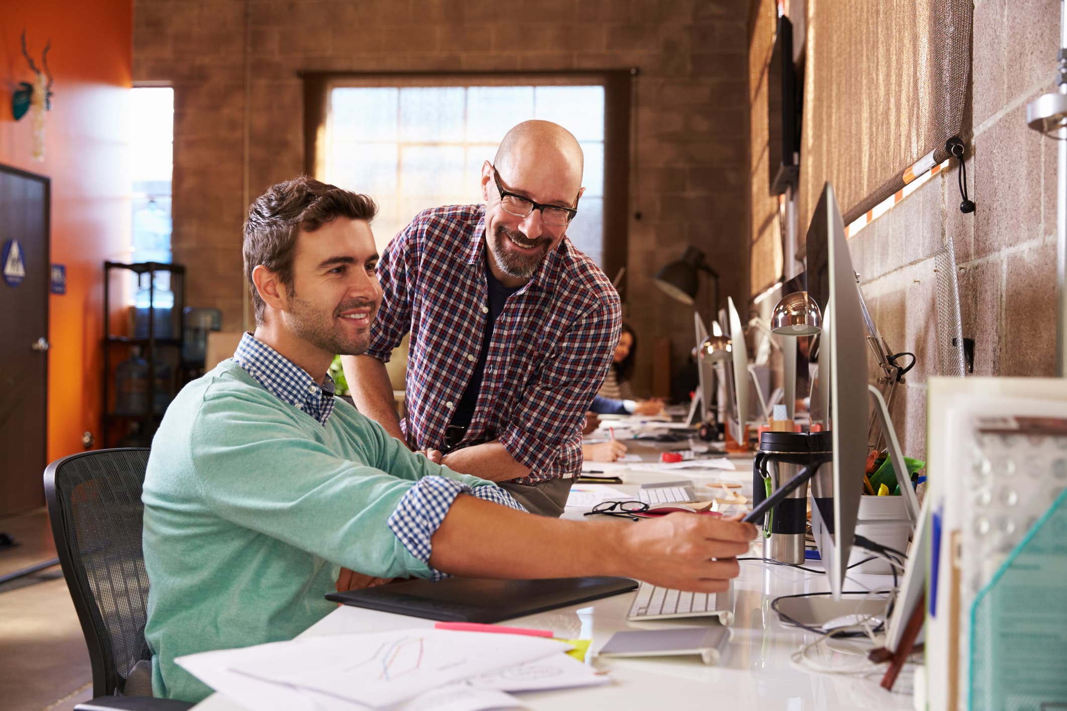 Two men smiling, collaborating on change management at a desk with computers in an office.
