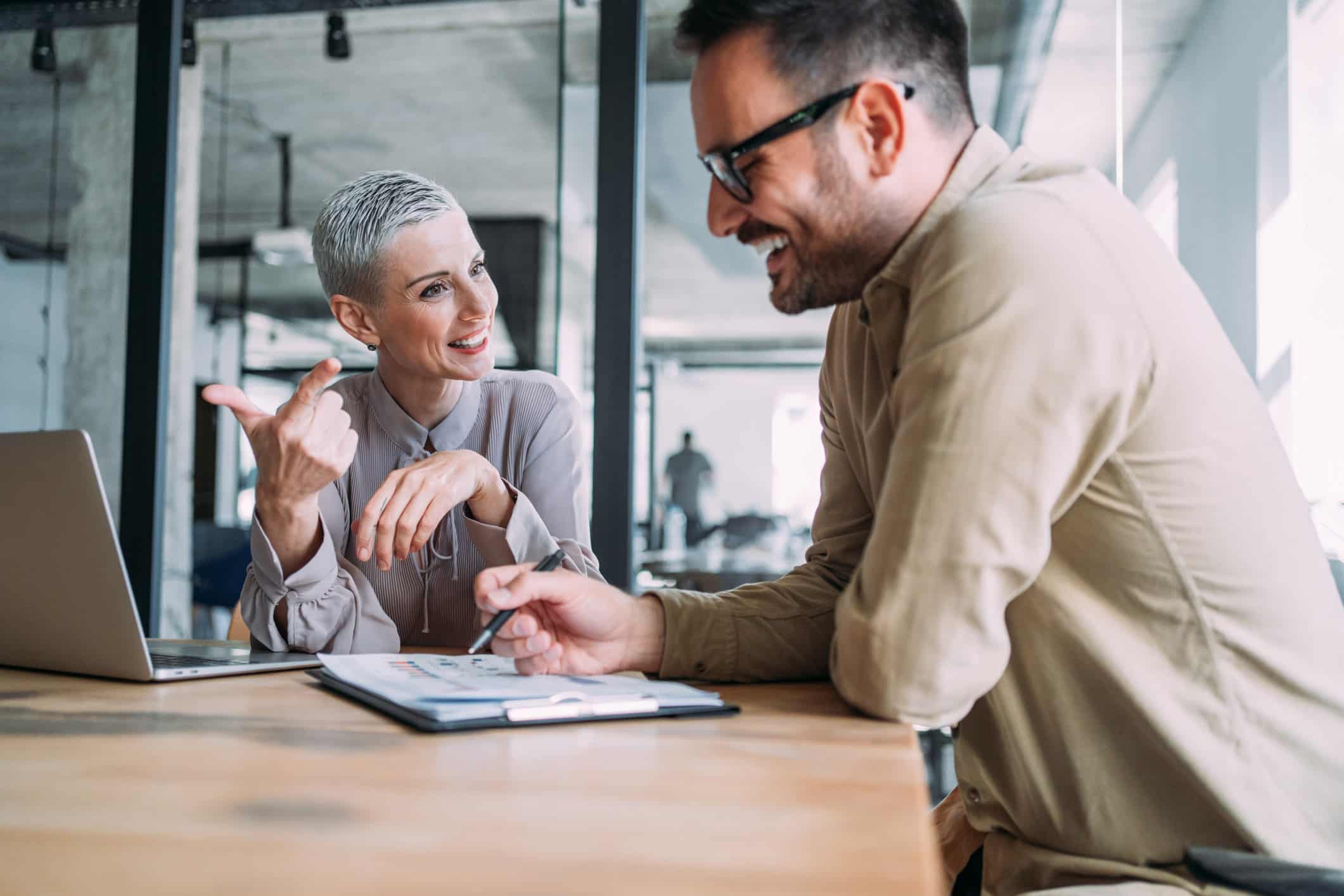 Two colleagues discuss change management and communication at a desk with a laptop in an office.