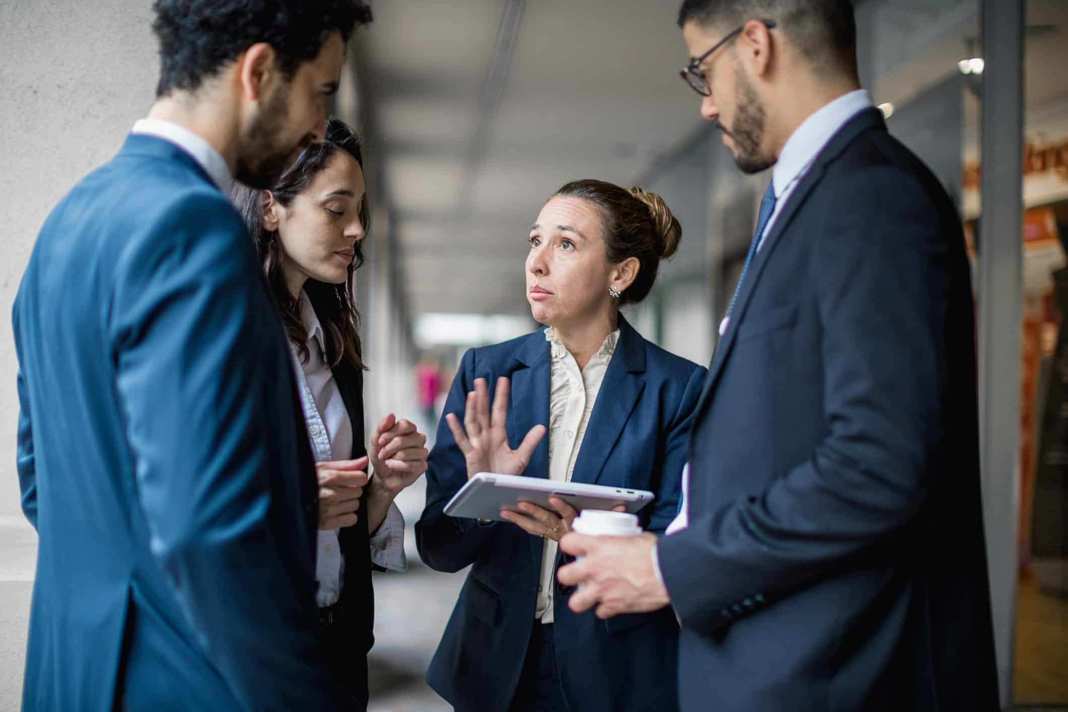 Four professionals in suits discuss law firm strategic planning outdoors, one holding a tablet.