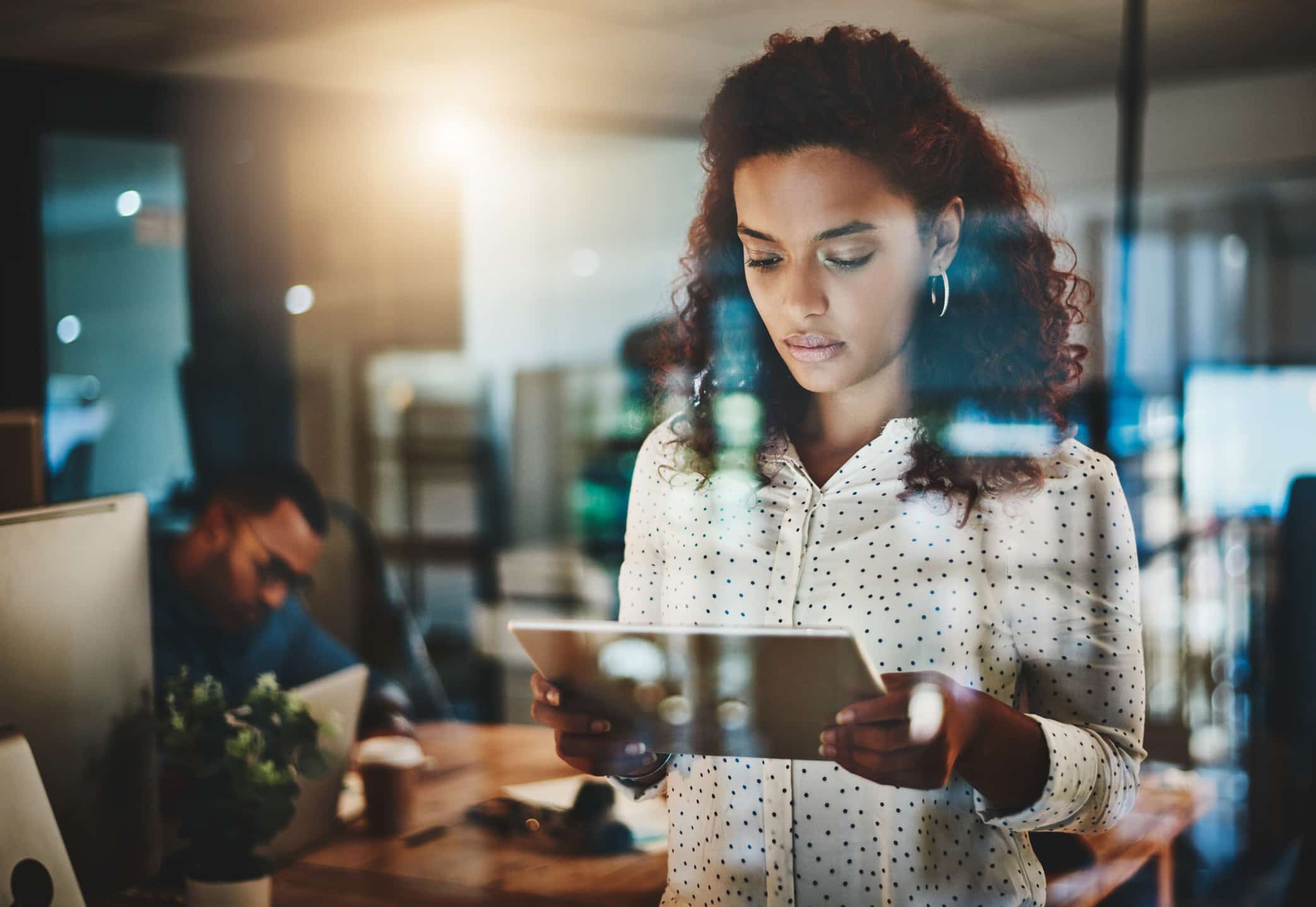 Woman in an office at a law firm growth consulting firm, viewing a tablet, coworker behind.