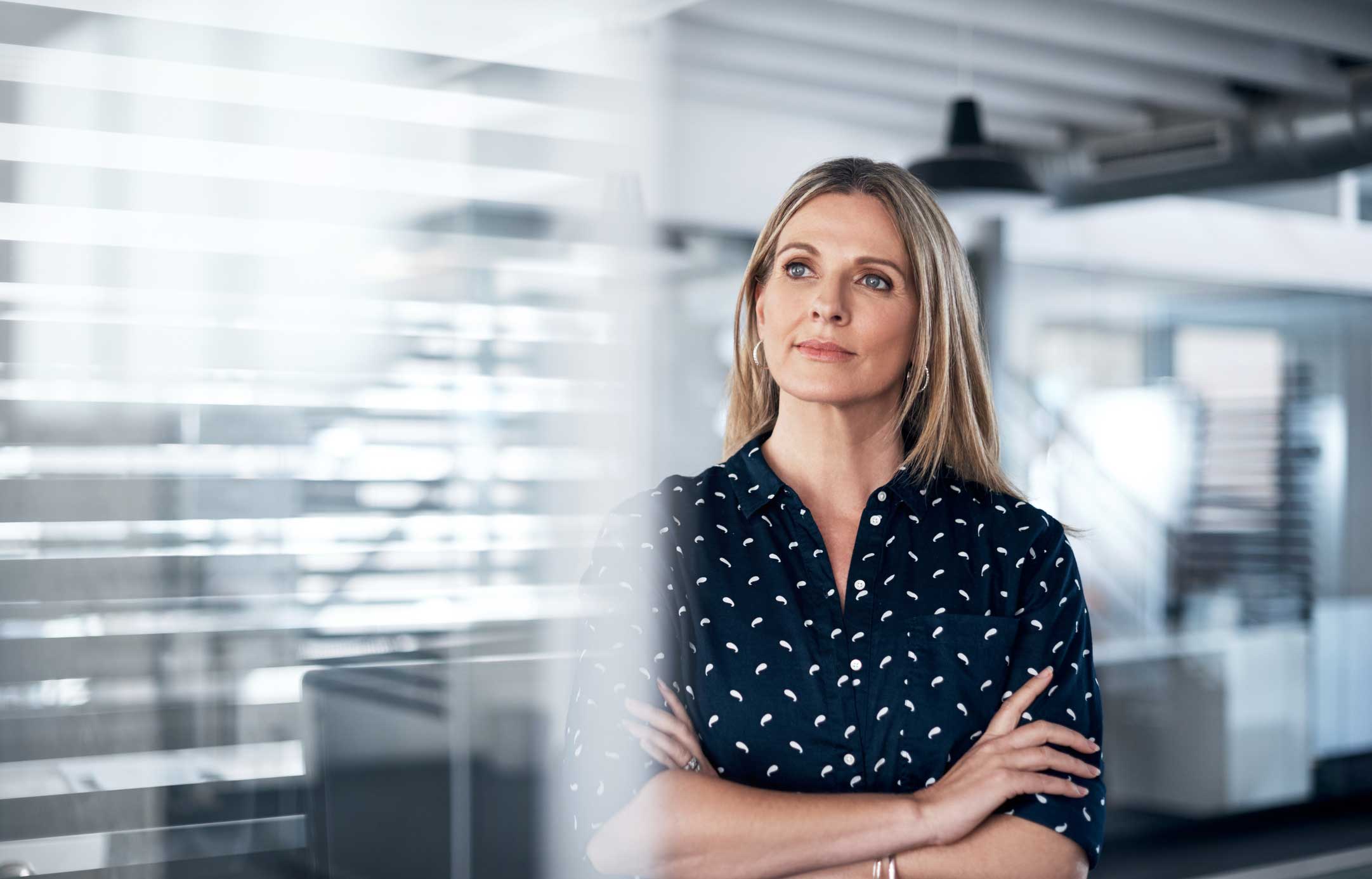 Woman with long blonde hair stands with arms crossed, reflecting on communication strategies.