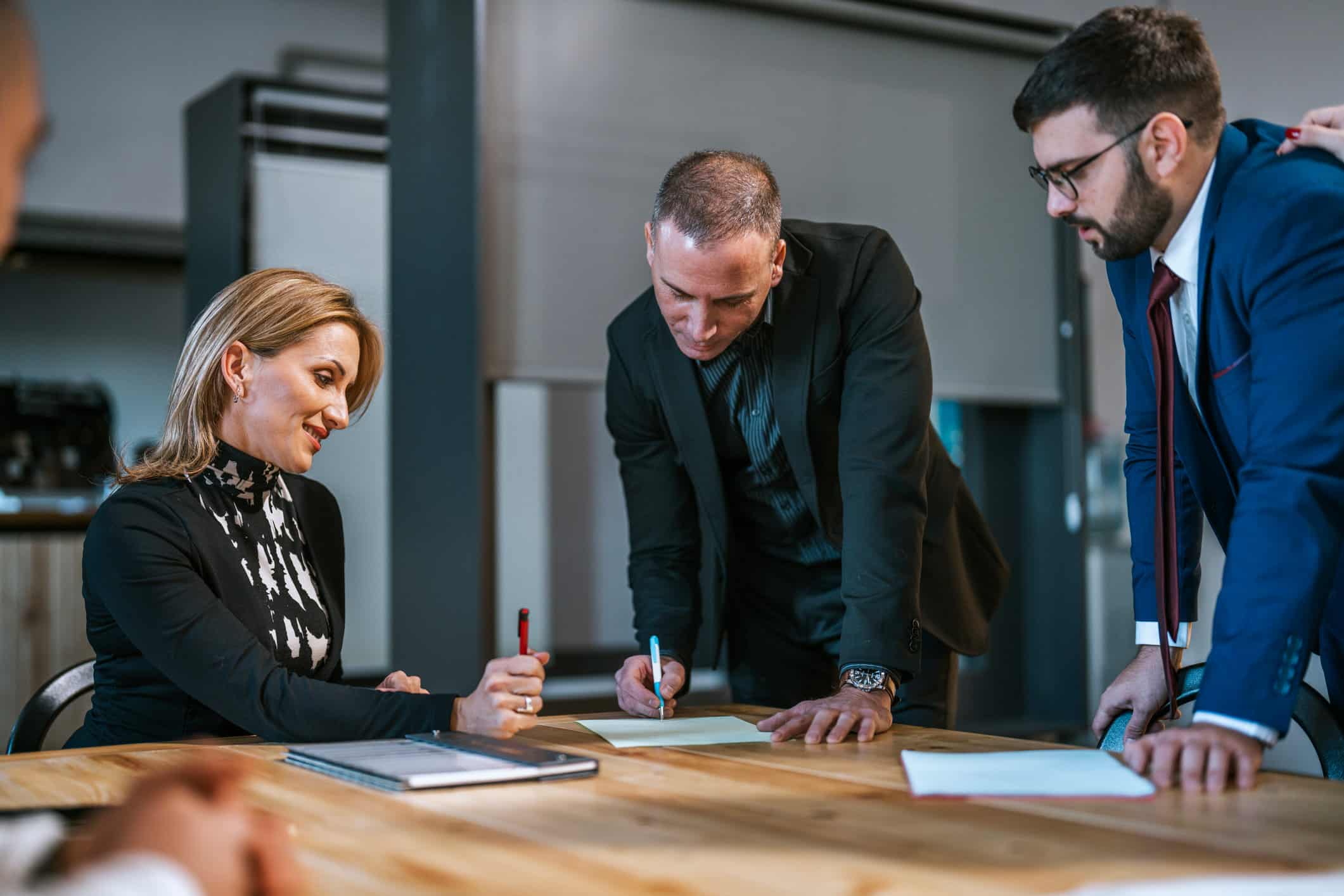 Three professionals discuss compensation strategy consulting while signing documents in a modern office.