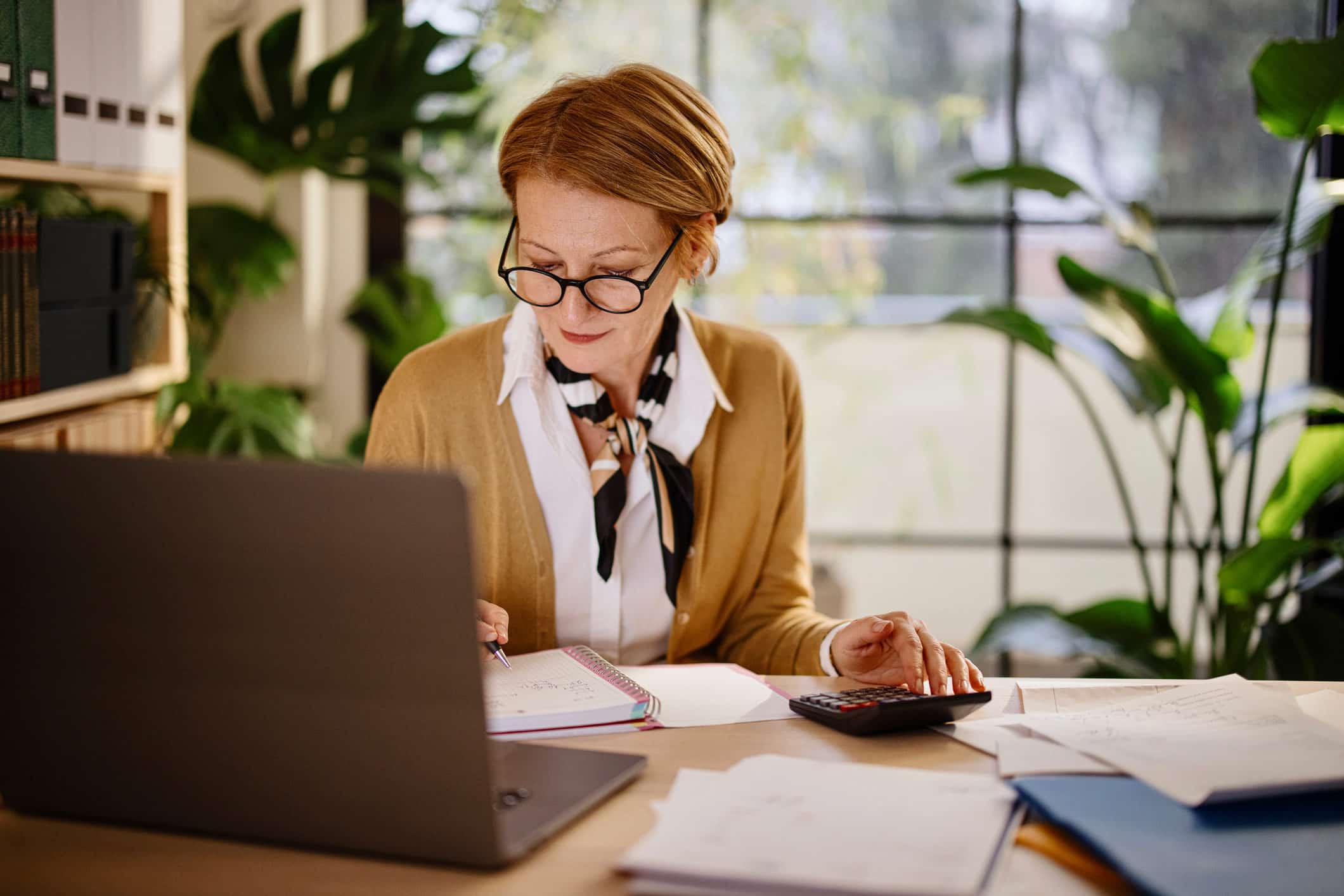 Woman working at desk on Business Valuation Consulting in a bright, plant-filled office.
