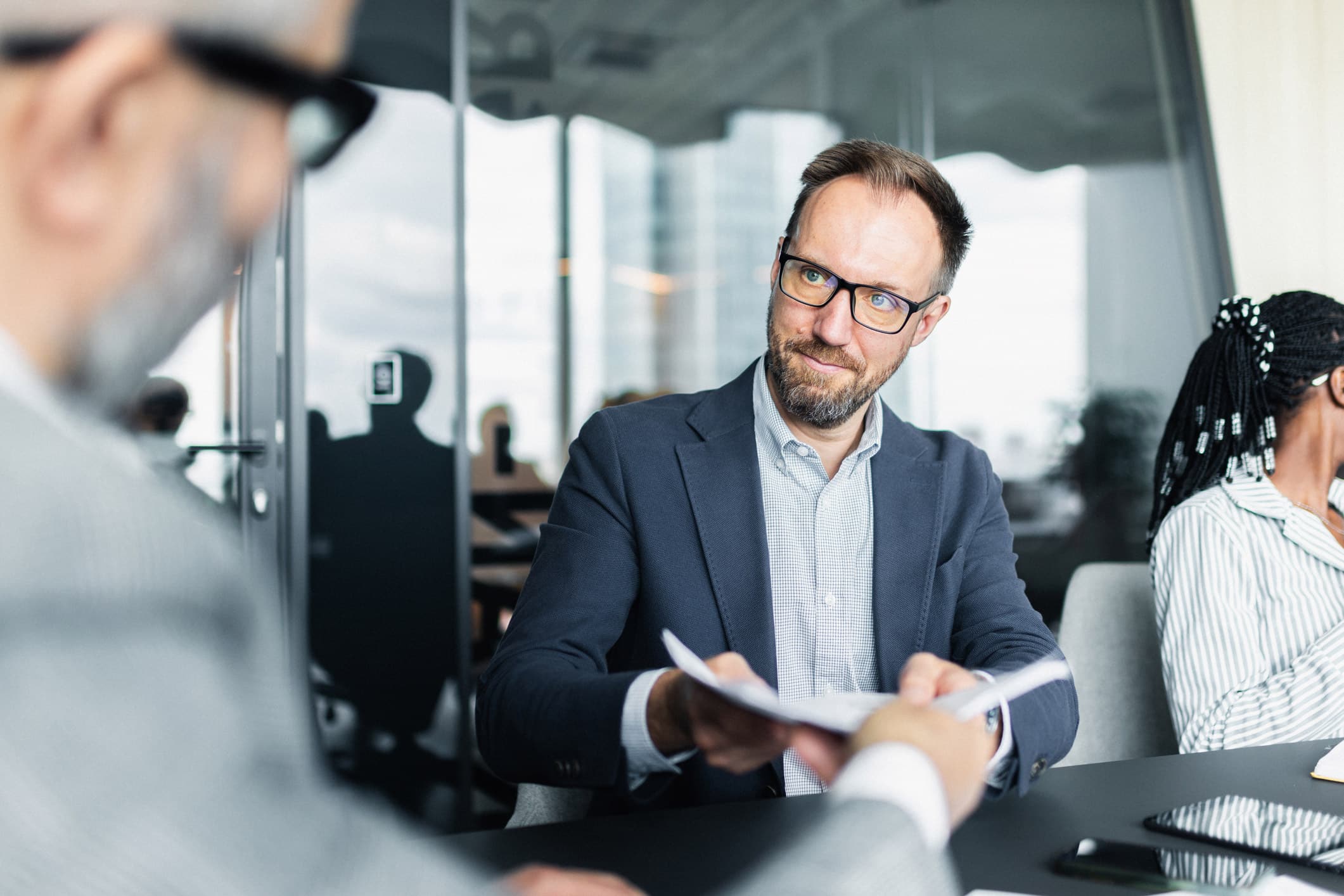 Man in glasses hands a document on Mergers & Acquisitions Advisory Services to a colleague.