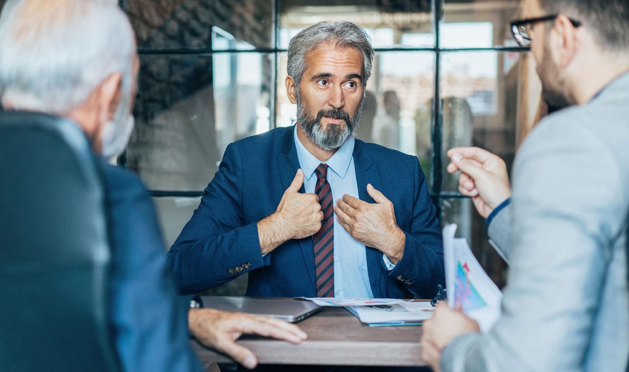 A man in a suit gestures while discussing Business Intelligence Advisory at a business meeting.