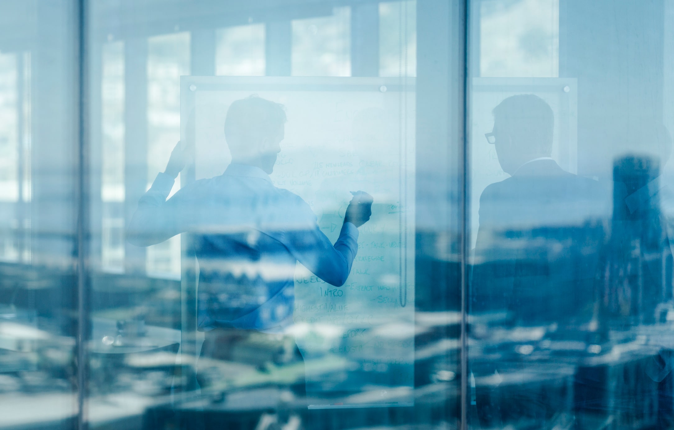 Two people discuss Continuous Active Learning Implementation at a whiteboard, seen through glass.