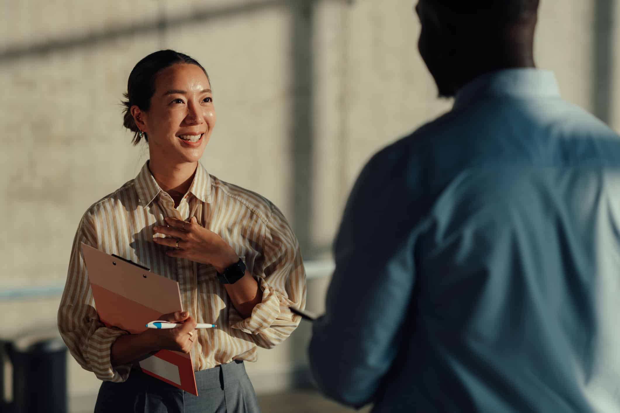 Smiling woman with a clipboard discusses Cross-Matter Intelligence in a bright indoor setting.