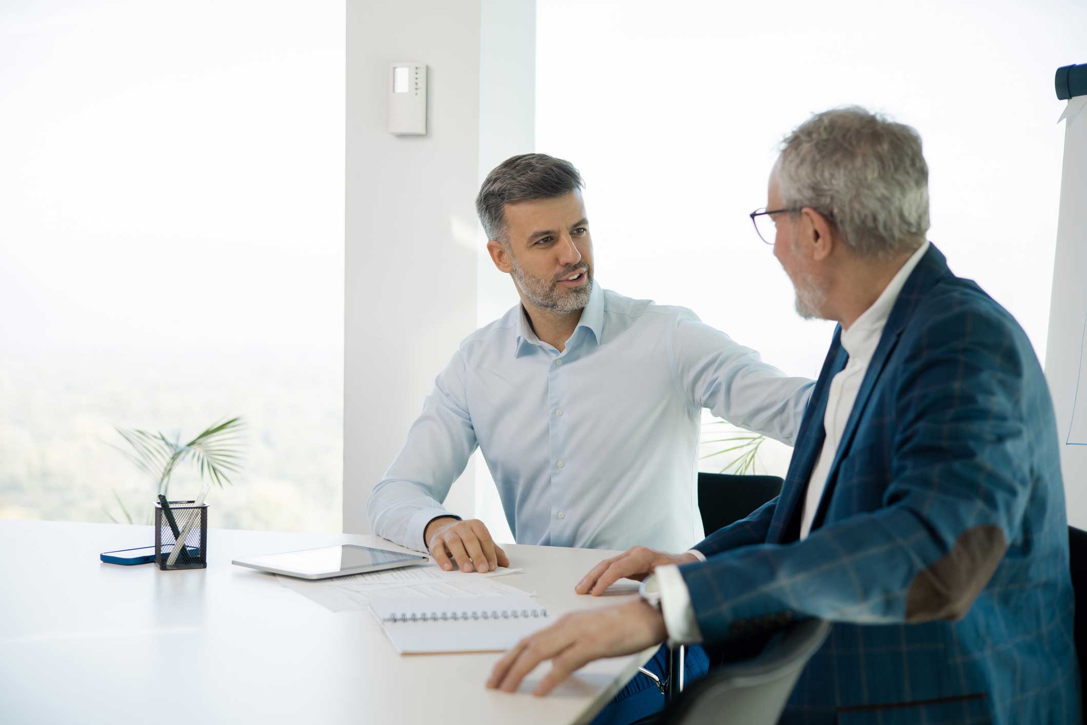 Two men in business attire discuss Cross-Matter Intelligence at a desk with notebooks and a tablet.