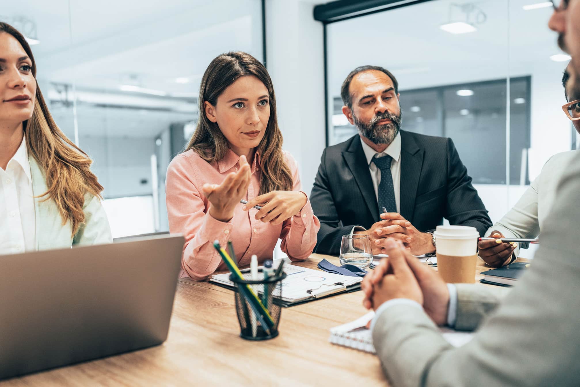 Four people discuss NLP Cultural Adoption in a business meeting with laptops and notebooks.
